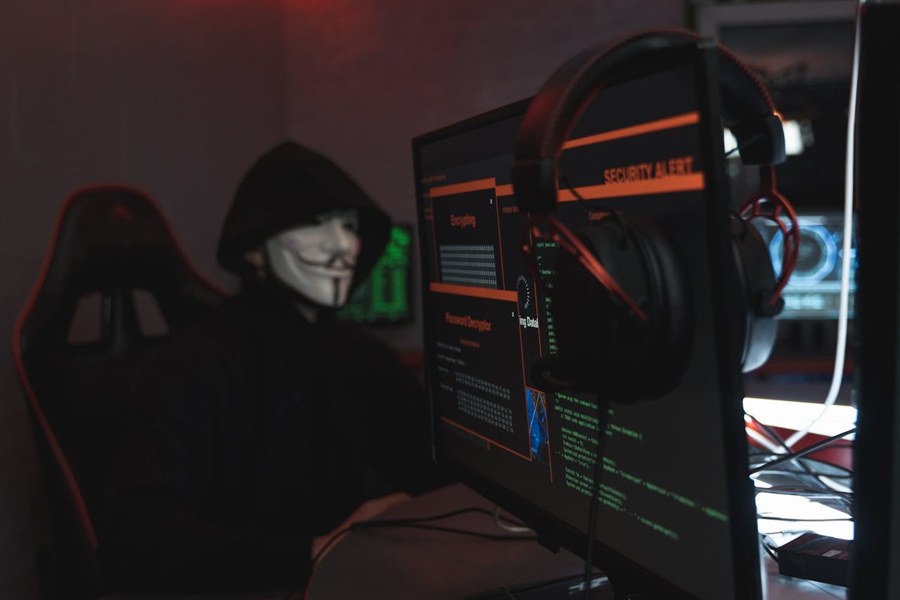 A person wearing a Guy Fawkes mask engaged in hacking activities on a computer in a dimly lit room.